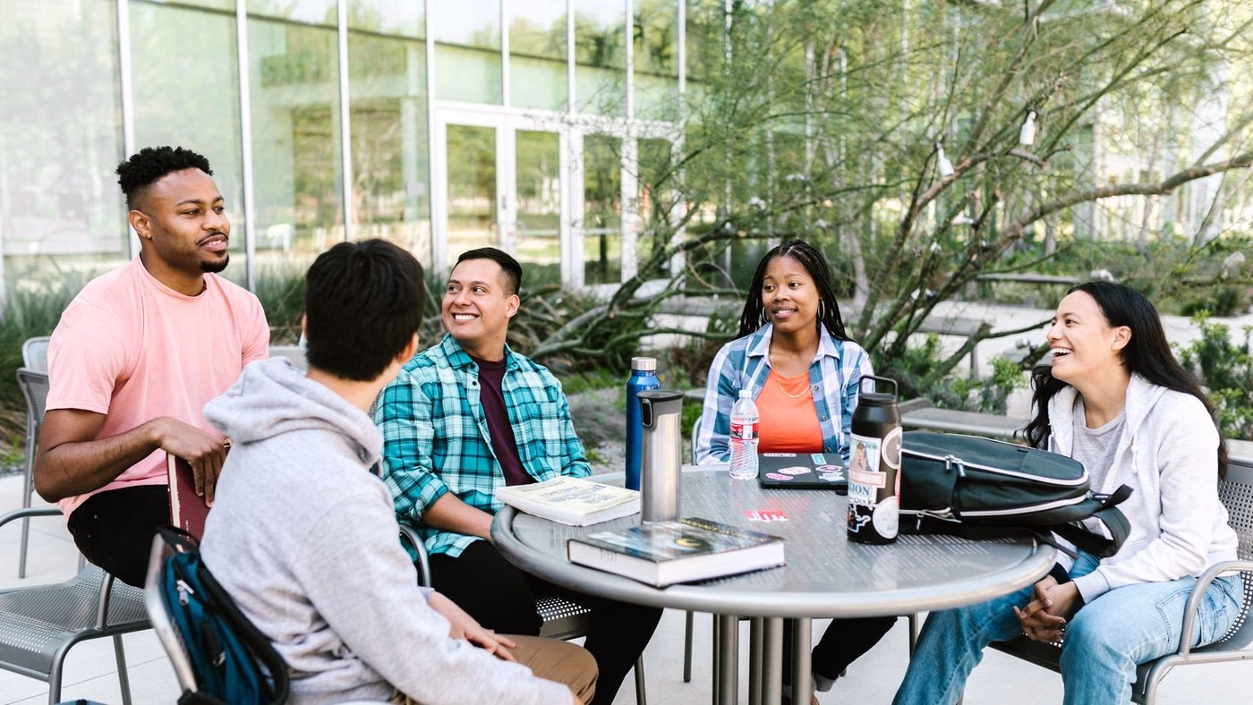 University students studying together outside at a campus table.