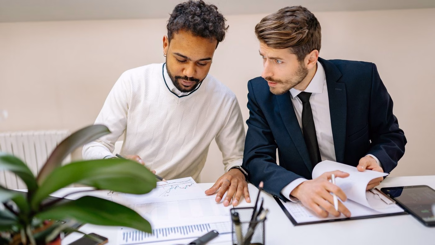 Two men in a modern office discussing and analyzing documents with charts.