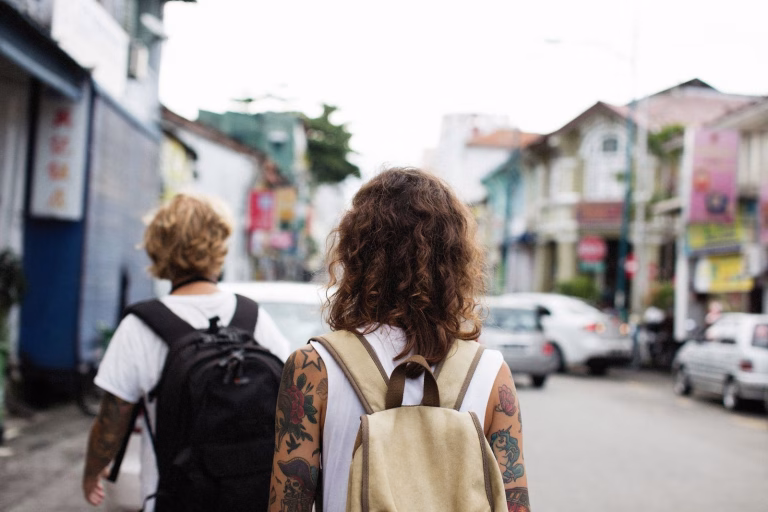 Travelers with backpacks walk down a lively city street, exploring the urban surroundings.