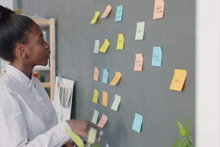 Focused young woman analyzing sticky notes on a chalkboard for project planning.