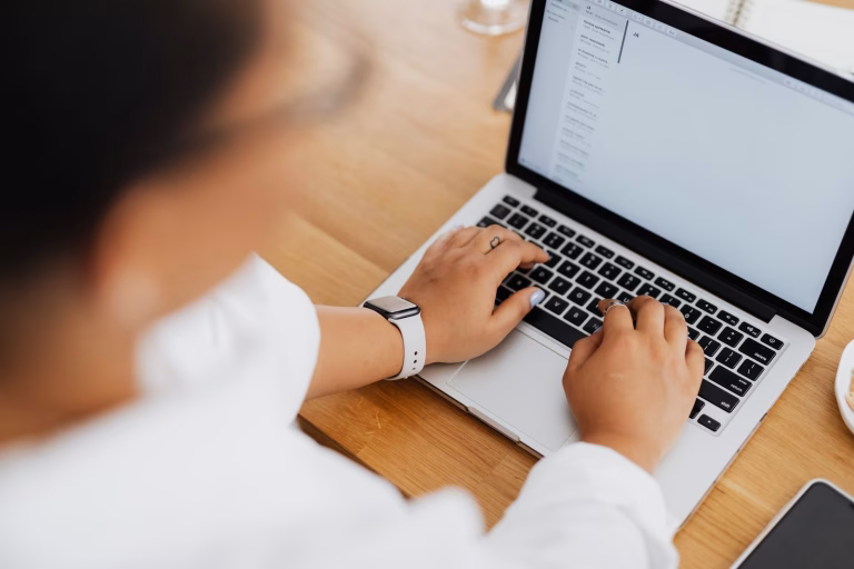 High angle shot of a person typing on a laptop, focused on hands and keyboard.