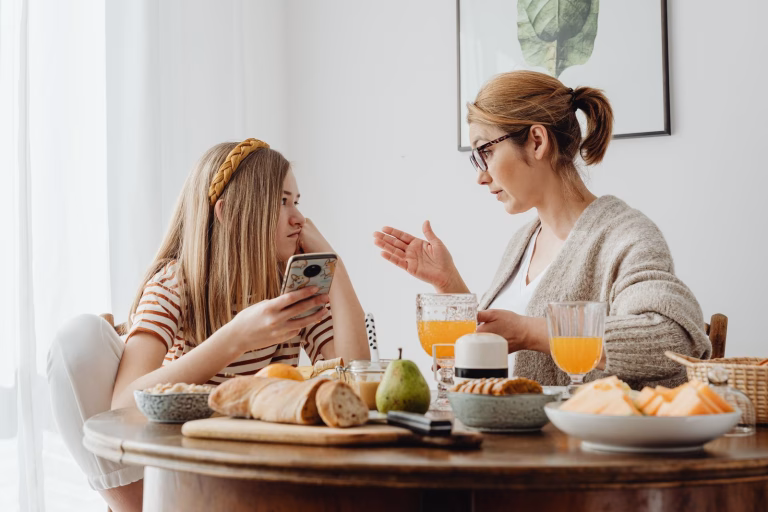 A mother and daughter engage in a conversation over breakfast, with an array of food on the table.