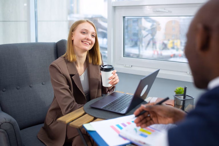 Two business professionals having a meeting in a modern office setting, enjoying coffee and smiles.