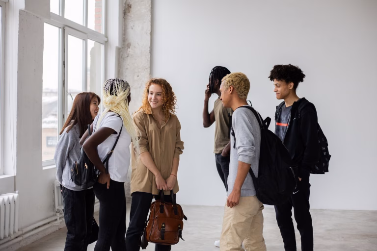 Group of positive multiracial students with backpacks discussing studying issues after work in team